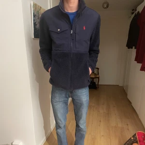 Mörkblå fleecejacka från Ralph Lauren - Säljer en snygg mörkblå fleecejacka från Ralph Lauren. Den har en dragkedja framtill och en bröstficka med knapp. Perfekt för höst och vinter, med en skön och varm känsla. Jackan har långa ärmar och en klassisk passform. Perfekt för både vardag och lite finare tillfällen. Skick 9/10 som ny, skriv vid frågor. Nypris 3000 kan passa storlek M också 