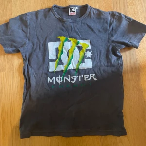 DC tröja - Säljer en grå t-shirt från DC Shoes med Monster Energy-logga i grönt och vitt på framsidan. Den är kortärmad och i bra skick, perfekt för vardagsbruk eller chill häng. Materialet känns mjukt och bekvämt. Passar bra till jeans eller shorts för en avslappnad stil! 💖