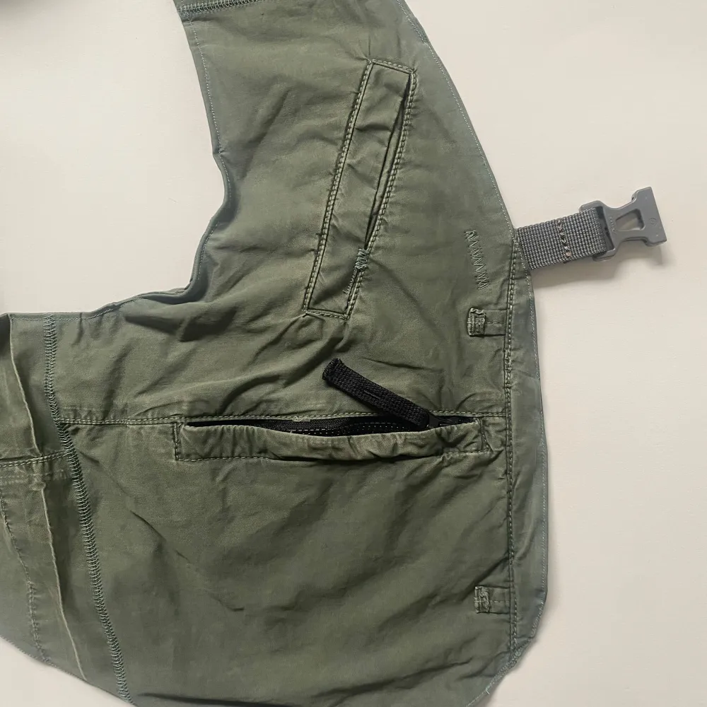 Säljer en cool grön axelväst från Stone Island. Axelvästen har en justerbar rem och en praktisk ficka med lock framtill. Perfekt för att bära dina nödvändigheter med stil. Den är omgjord av mig från en par Junior Stone Island pants. Axelväst modellen efterliknar Engineered Garments shoulder väst.. Asusteet.
