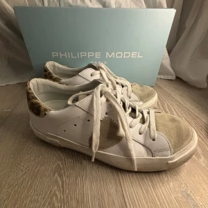 Philippe Model sneakers med leoparddetaljer - Säljer mina as snygga Philippe Model sneakers i vitt skinn med coola leoparddetaljer på hälen. Skorna har snörning och en snygg beige mockadetalj på sidan. Köpta för ca 3 månader sedan, men använda ca 5 ggr. Säljer då de inte kommer till användning. Pris kan diskuteras😇