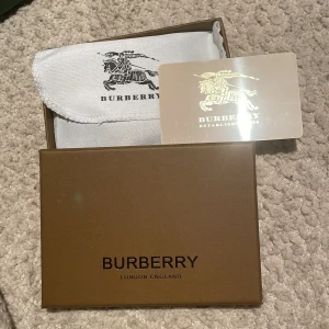 Cardholder från burberry  - Säljer ett snyggt och stilrent kortfodral från Burberry i deras klassiska rutiga mönster. Fodralet är i beige och svart med Burberry-loggan tryckt på framsidan. Perfekt för att hålla dina kort organiserade med stil. Kommer i originalförpackning med dustbag och certifikat.