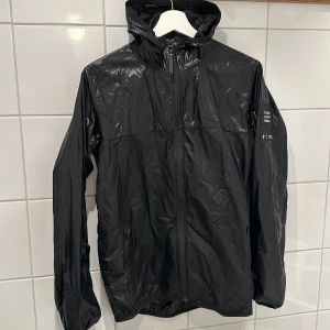 Svart vindjacka från Peak Performance - Säljer en svart vindjacka från Peak Performance i mycket bra skick. Jackan har en praktisk huva och dragkedja framtill. Perfekt för blåsiga dagar och passar bra till både vår och höst. Stilren design med Peak Performance-logga på ärmen. Stl 170