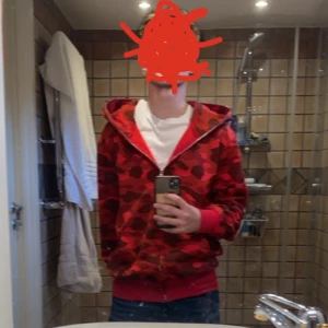 Röd BAPE  - Säljer en cool röd Bape. Den har dragkedja och broderade detaljer som ger en unik look. Perfekt för höst och vår, och den är i mycket bra skick. Passar perfekt för streetwear-stilen! I storlek S men passar även M.