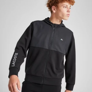 Svart hoodie från Lacoste - Säljer en snygg svart hoodie från Lacoste och är oanvänt och den är inte ens öppnas från packetet . Den har en dragkedja framtill och det klassiska Lacoste-märket på bröstet. Perfekt för höst och vår, med långa ärmar och en bekväm passform. Lacoste-loggan finns även på ärmen. Perfekt för både träning och vardag!