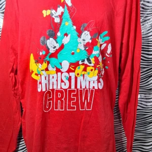 Röd jultröja med Disney-motiv - Säljer en superfin röd jultröja med Disney-motiv. Perfekt för julfirandet med 'Christmas Crew' tryckt på framsidan. Tröjan har långa ärmar och är gjord i ett mjukt material. Perfekt för att sprida julstämning! 🎄