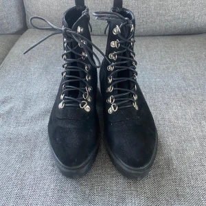 Svarta boots med snörning - Säljer ett par snygga svarta boots i mocka med snörning och dragkedja på sidan. De har en rejäl sula som ger bra grepp och en cool look. Perfekta för höst och vinter, både stiliga och praktiska. Passar till både jeans och kjol!
