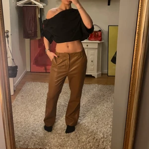 Bruna byxor i skinnimitation - Säljer ett par snygga bruna byxor i skinnimitation. De är högmidjade och har en straight passform som ger en stilren look. Perfekta för höst och vinter, och kan enkelt kläs upp eller ner beroende på tillfälle. Byxorna har en dragkedja och knapp framtill.