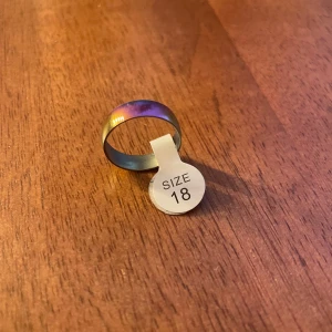 Färgglad ring i storlek 18 - Säljer en cool ring i storlek 18 med en skimrande färg som skiftar mellan lila och guld. Perfekt för att ge lite extra stil till din outfit. Ringen har en slät yta och är bekväm att bära. Passar både till vardags och fest!