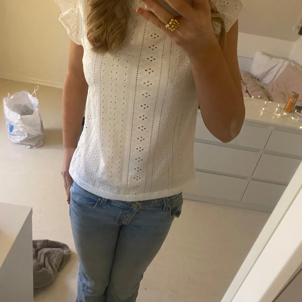 Säljer en söt vit blus med spetsdetaljer och korta ärmar. Perfekt för sommardagar eller en avslappnad vårlook. Blusen har ett fint hålmönster och volangdetaljer vid ärmarna. Passar bra till jeans eller kjol för en chic stil.. Toppar.