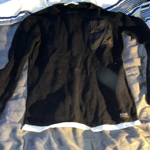 Svart långärmad tröja från H&M - Säljer en svart långärmad tröja från H&M i bra skick. Tröjan har en enkel design med en liten bröstficka och är perfekt för både höst och vinter. Den är gjord i ett bekvämt material som håller dig varm. Perfekt för vardagsbruk!