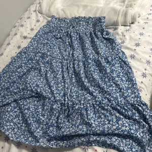 Blå blommig kjol - Superfin blå långkjol med vitt blommönster. Perfekt för sommardagar eller en mysig vårutflykt. Den har en elastisk midja för extra komfort och en luftig passform. Kjolen är i mycket bra skick och redo för nya äventyr! 🌸