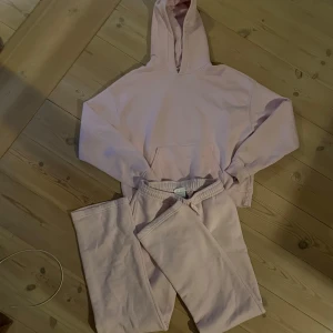 Rosa hoodie och mjukisbyxor - Säljer ett set med en supermjuk rosa hoodie och matchande mjukisbyxor. Perfekt för mysiga dagar hemma eller en avslappnad dag ute. Hoodien har en klassisk känguruficka och byxorna har en bekväm dragsko i midjan. Ginatricot 