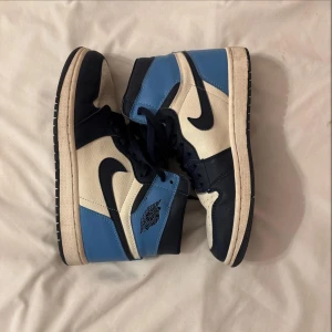 Nike Air Jordans i blått och vitt - Säljer ett par Nike Air Jordan 1s Obsidian i snygg blå och vit färgkombination. Skorna har klassisk snörning och den ikoniska Nike-loggan på sidan. Perfekta för både vardag och speciella tillfällen. Ikonisk modell och colorway.  De är i mycket bra skick och redo för en ny ägare!
