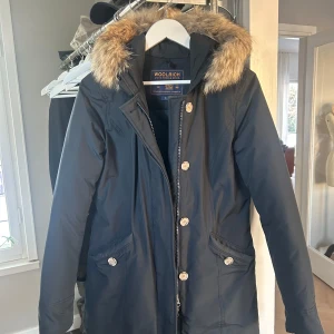 Mörkblå parkajacka från Woolrich - Säljer en snygg mörkblå parkajacka från Woolrich i storlek S. Jackan har en avtagbar huva med päls och stängs med både dragkedja och knappar. Perfekt för kalla vinterdagar! Den fungerar även för de som har XS. Nypris 9000