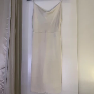 Klänning - Säljer en elegant vit klänning med smala axelband. Den är perfekt för sommarens fester eller en fin middag. Klänningen har en enkel och stilren design som ger en sofistikerad look. 