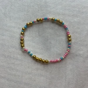 Färgglatt armband och guldfärgat halsband - Säljer ett färgglatt armband med pärlor i guld, rosa och blått samt ett matchande guldfärgat halsband. Armbandet är elastiskt och passar de flesta handleder. Perfekt för att liva upp vilken outfit som helst! 🌟