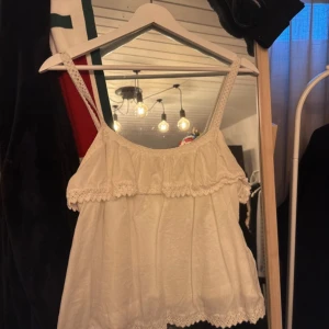 Vit spetslinne från Bik Bok - Säljer ett superfint vitt linne från Bik Bok. Det är ärmlöst med smala axelband och har vackra spetsdetaljer både upptill och nedtill. Perfekt för sommardagar eller en avslappnad festkväll. Passar bra till jeans eller kjol!