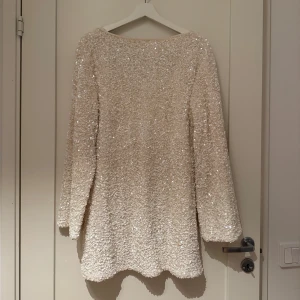 Vit glittrig klänning med svart rosett - Säljer en superfin vit glittrig klänning med lång ärm och en stor svart rosett i ryggen. Från H&M använd 1 gång! 