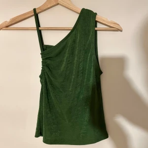Grön oneshoulder topp - Skön och stretchig topp från Mango. Lite glittrig i tyget, färgen är mer korrekt på andra bilden. Knappt använd men jättefin!