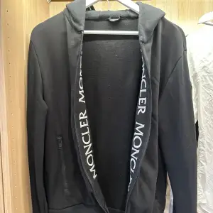 Säljer en svart hoodie från Moncler i mycket bra skick. Den har en dragkedja framtill och långa ärmar. Moncler-loggan syns på insidan av luvan. Inköpt jul 2020. Nypris 13000. Kvitto finns.