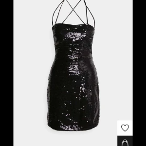 Nyårsklänning  - Snygg svart paljettklänning med öppen rygg och smala axelband. Perfekt för nyår tillfällen! Klänningen är kort och har en tight passform som framhäver figuren. Den glittriga ytan gör den till ett riktigt statement-plagg.