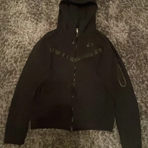 Nike tech fleece  - Säljer min svarta Nike tech, den är i väldigt bra skick. Den har en dragkedja framtill och en praktisk huva. Perfekt för höst och vår, eller när du bara vill ha något bekvämt och stilrent. Passar både till träning och vardag.