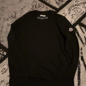 Svart tröja från Moncler - Säljer en stilren svart tröja från Moncler. Den har en klassisk design med långärmade ärmar och Monclers logga på ärmen. Perfekt för både vardag och festliga tillfällen. Passar bra till höst och vinter.