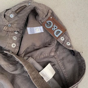 Bruna cargobyxor från Dolce & Gabbana - Säljer ett par otroliga vintage bruna cargobyxor från Dolce & Gabbana. Svåra att hitta, speciellt i detta skick. Byxorna har flera fickor och knappar längs benen, och ett linnematerial, vilket gör de väldigt sköna på vår och sommar. Passar bäst till xs-s om man vill ha en baggy look. Perfekta för en avslappnad stil med en touch av lyx. Passar bra till både vardag och fest.