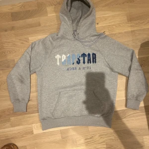 Grå och ljusblå hoodie från Trapstar - KAN GÅ NER I PRIS FÖR SNABB AFFÄR. Säljer en grå hoodie från Trapstar i bra skick. Den har en stor broderad text i blå och vit på framsidan. Hoodien är gjord av fleece i insidan och perfekt för kyliga väder. Perfekt för både vardag och chill. Använd max 5 gånger. skick 9,5/10. MVH Elt.wear