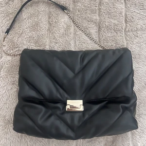 Svart quiltad axelväska med guld kedja ZARA - Snygg svart axelväska i quiltat skinn med en guld detaljer. Väskan har metallspänne framtill. Inga missfärgningar på guldet och väskan är i nyskick. Den är från Zara och är knappt använd. Mellanstor, perfekt för både vardag och fest! 🤩🖤