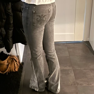 Grå jeans med broderad bakficka - Säljer ett par snygga grå jeans i bra skick. De har en cool broderad detalj på bakfickan och en bootcut-stil som ger en retro vibe. Perfekta för höst och vår! Passformen är normal och de är lågmidjade. 