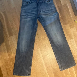 Coola jeans med unik stil - Säljer ett par feta blå jeans i bra skick. De har en klassisk rak passform. Jeansen har en mörk tvättad look med veckdetaljer vid låren och knäna. Mått finns på bilderna. 