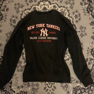Svart New York Yankees sweatshirt - Säljer en svart/mörkgrå sweatshirt med New York Yankees-tryck i rött och vitt. Tröjan har långa ärmar och är perfekt för en avslappnad stil. Den är i bra skick och passar både till vardags och sportiga tillfällen.