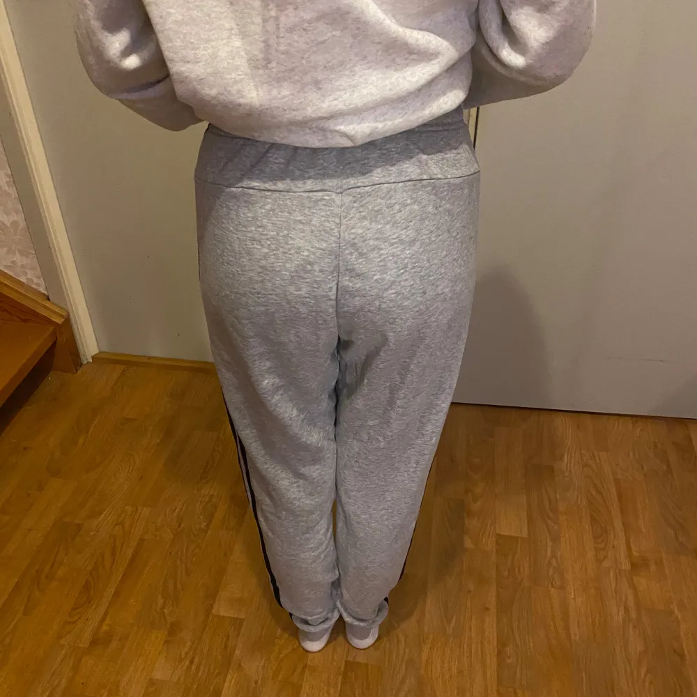 Säljer ett par grå mjukisbyxor från Adidas i mycket bra skick. De har en normal passform med klassiska svarta ränder längs sidorna och en elastisk midja. Perfekta att ha som mjukisbyxor eller träning. Notera att smörerna saknas.. Farkut & Housut.