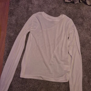 Vit långärmad tröja från 157 - Säljer en enkel och stilren vit långärmad tröja från 157. Perfekt för lager-på-lager under höst och vår. Tröjan är gjord i en mjuk blandning av polyester och viskos, vilket gör den både bekväm och lätt. Passar till både vardag och avslappnade tillfällen.