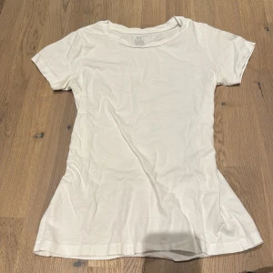 Vit t-shirt från Kappahl - Säljer en vit t-shirt från Kappahl i storlek XS. Den är gjord av ekologisk bomull och har en klassisk design med korta ärmar. Perfekt basplagg för alla tillfällen!