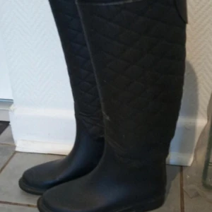 Svarta quiltade stövlar - Säljer ett par svarta quiltade stövlar i bra skick. De är perfekta för höst och vinter med sitt stilrena och praktiska design. Stövlarna är tillverkade i syntetmaterial och har en bekväm passform. Perfekta för att hålla fötterna torra och varma under regniga dagar. De är även smala vid vaden 