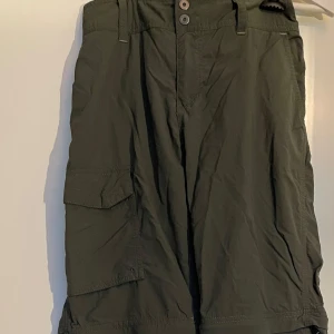 Gröna cargobyxor från Columbia - Säljer ett par gröna cargobyxor från Columbia i mycket bra skick. De har flera praktiska fickor, går att göra till shorts genom att ta av nedre delen med dragkedja. Går också att enkelt spänna ut och in i midjan. 