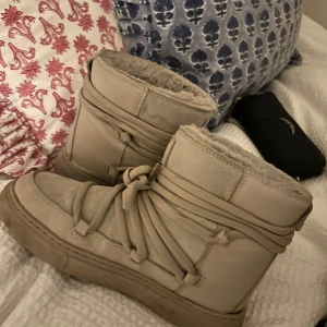 Inukii liknade skor  - Säljer ett par snygga beige boots från H&M i storlek 36. De har en cool snörning och är perfekta för höst och vinter. Skorna är i bra skick och har en mysig insida som håller fötterna varma. Perfekta för att hålla stilen när det blir kallt ute! Med några få defekter!!