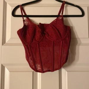 Röd spetskorsett från H&M - Snygg röd korsett från H&M i spetsmaterial. Den har justerbara axelband och hakknäppning bak. Perfekt för en festlig kväll eller en speciell tillställning. Korsetten har en vacker blommig spetsdesign som ger en elegant touch. Inge defekter eller liknande ❤️