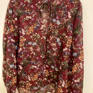 Blus strl S  - Burgundy / vinröd blommig blus i storlek S. Material: polyester. Lite genomskinligt tyg. Mycket fint skick. 