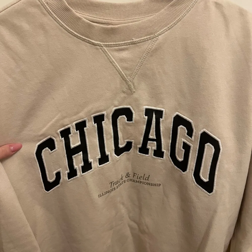 Säljer en snygg beige sweatshirt med stort 'CHICAGO' tryck på framsidan. Perfekt för en casual look eller att mysa i hemma. Tröjan har långa ärmar och en klassisk rund halsringning. Den är i bra skick och superbekväm att ha på sig. Passar perfekt till jeans eller leggings! Från h&m och i storlek S. Tröjor & Koftor.