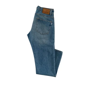 Blå jeans från Woodbird - Säljer ett par snygga blå jeans från Woodbird i modellen Doc Van. De är i en autentisk blå färg och har en klassisk femficksdesign. Passar till alla tillställningar! Knappt använda