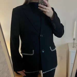 Oversized kavaj med vita sömmar - Snygg svart kavaj med vita sömmar som ger en cool kontrast. Den har en klassisk passform med knappar framtill och långa ärmar. Perfekt för både vardag och fest!