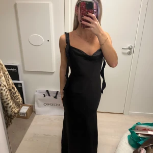 Svart långklänning med öppen rygg - Superfin klänning i satin från ginatricot! Aldrig använd och har därför prislapp kvar! Strl XS! Nypris: 600kr