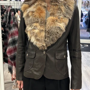 Brun äkta skinnjacka med pälsdetaljer - Säljer en snygg italiensk brun skinnjacka med en lyxig pälsdetalj runt kragen. Jackan har långa ärmar och knappar framtill. Perfekt för höst och vinter när du vill hålla dig varm och stilren. Passar både till vardags och fest!