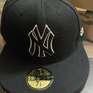 Svart keps från New Era - Snygg svart keps från New Era med broderad logga framtill. Perfekt för både vardag och sportiga tillfällen. Kepsen har en klassisk design med platt skärm och är i mycket bra skick. Passar perfekt för dig som gillar stilrena accessoarer.