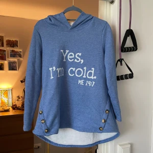 Blå hoodie med text - Mysig blå hoodie med texten 'Yes, I'm cold. ME 24:7' på framsidan. Den har en fluffig vit insida som håller dig varm och knappar som dekorativ detalj på sidorna. Perfekt för kyliga dagar! Helt ny