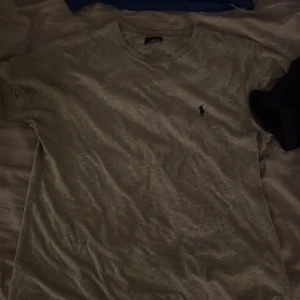 Grå t-shirt från Ralph Lauren - Säljer en klassisk grå t-shirt från Ralph Lauren i 100% bomull. Den har en liten broderad logga på bröstet och är perfekt för en avslappnad stil. Passar både till vardags och lite finare tillfällen.