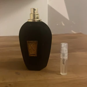 Svart parfymflaska med gulddetaljer 2 ml - Säljer en elegant svart parfymflaska med gulddetaljer. Flaskan har en lyxig känsla med en guldig spraytopp och en rektangulär guldplatta på framsidan. Perfekt för den som vill ha en sofistikerad doftupplevelse. Inkluderar även en liten genomskinlig sprayflaska för resor eller prov.     2 ml